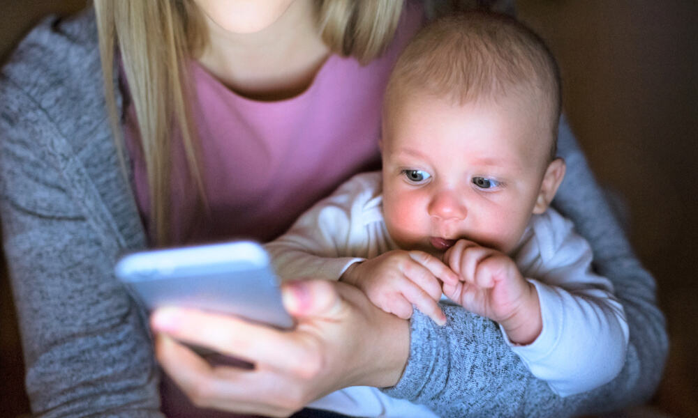 Smartphone addiction- image of mom using smartphone with baby on lap