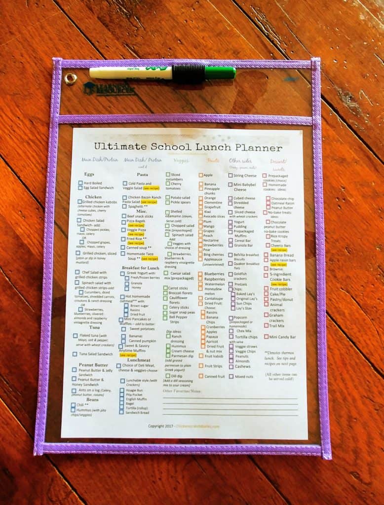 Image of the printable Ultimate School lunch planner in a clear sleeve, on a wooden table
