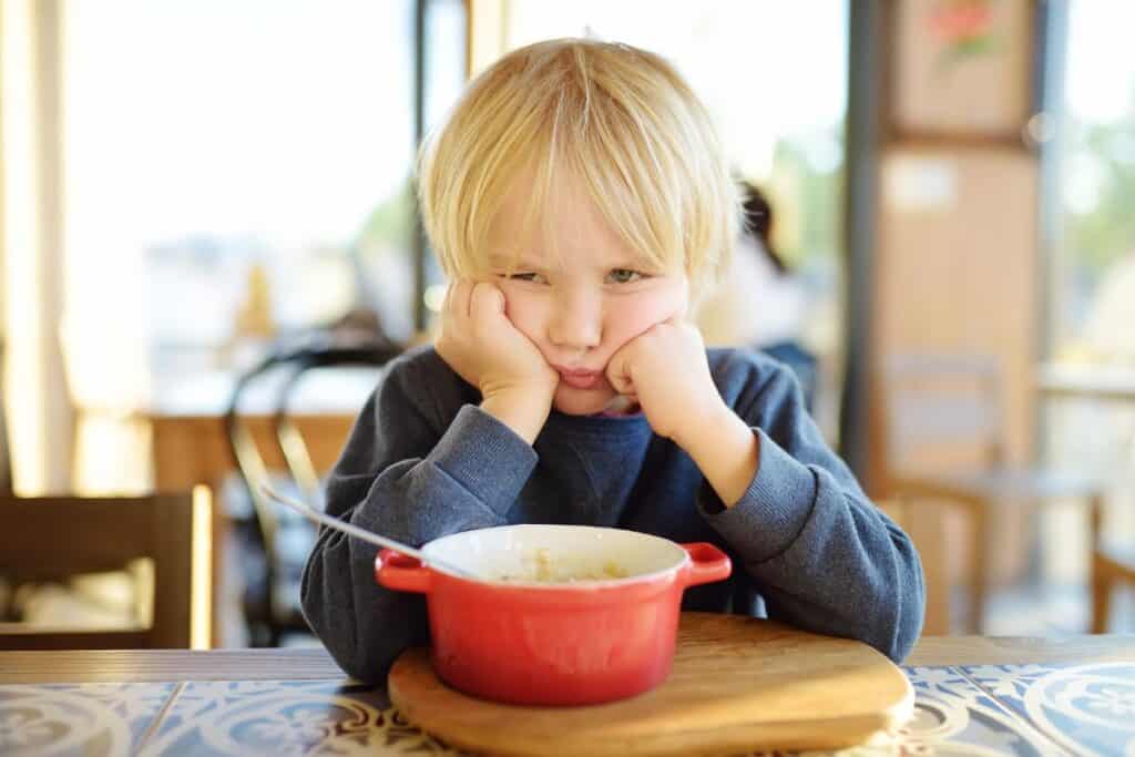 Little boy frowning over a red bowl at the dinner table.