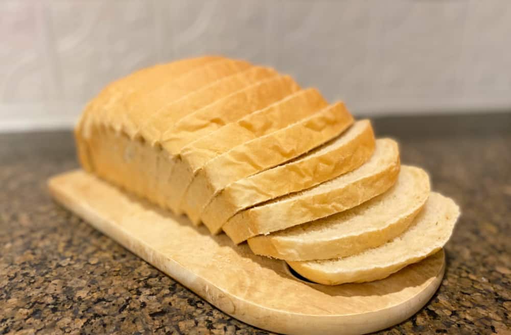 Sliced homemade sandwich bread on a cutting board sitting on a granite countertop.