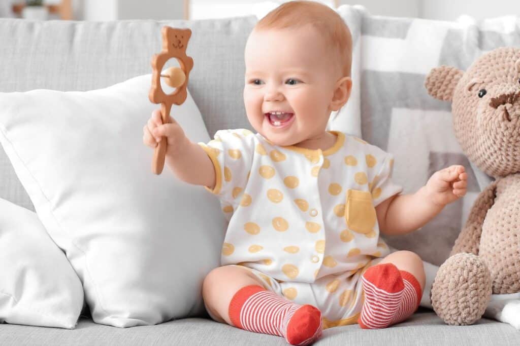 Happy baby sitting on couch playing with natural wooden toy