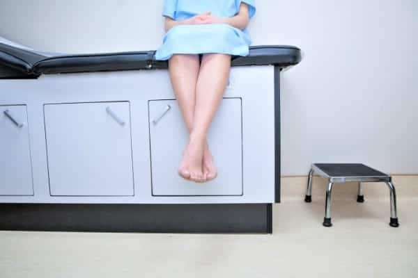 Productive Things to Do While You're Waiting: a woman sitting on an exam table in a hospital gown.