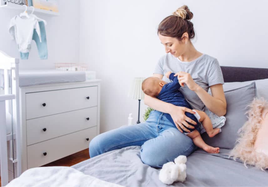 New mom breastfeeding at home in baby's grey and white nursery.