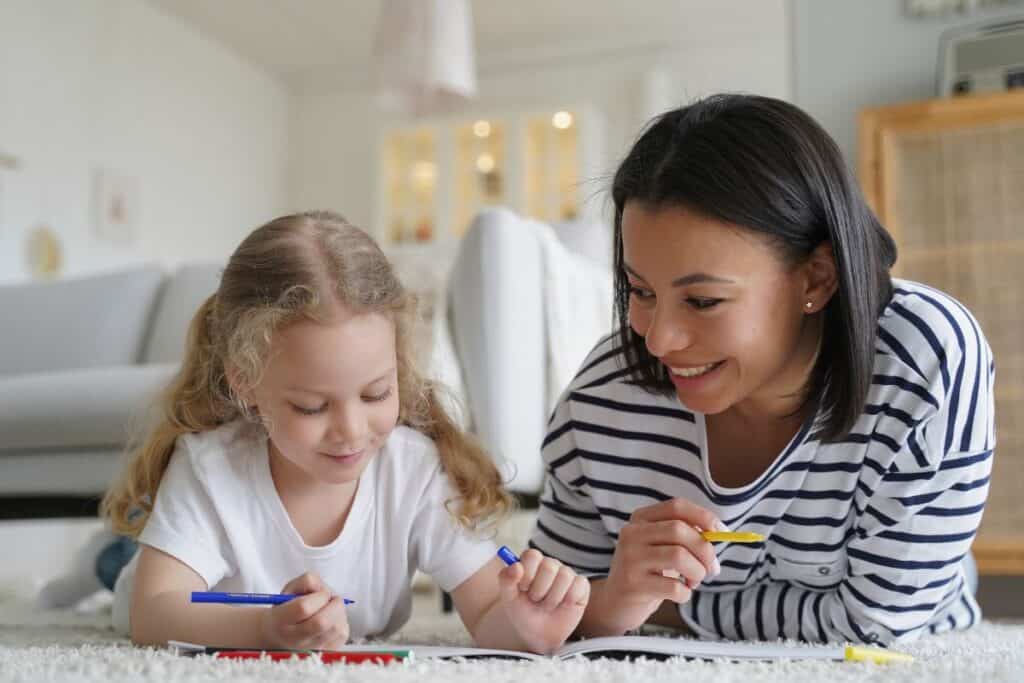 Mom and daughter coloring together on living room floor.