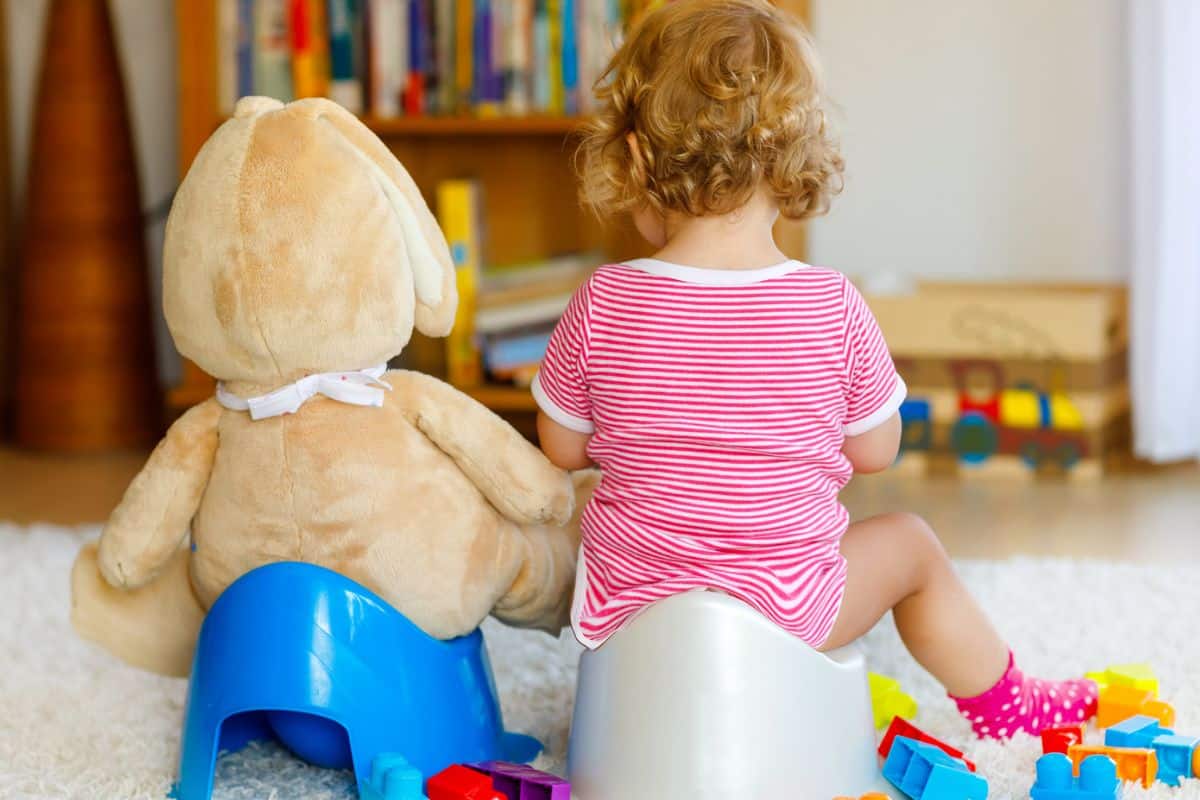 Stubborn toddler potty training in living room with toy next to her in potty chair too.
