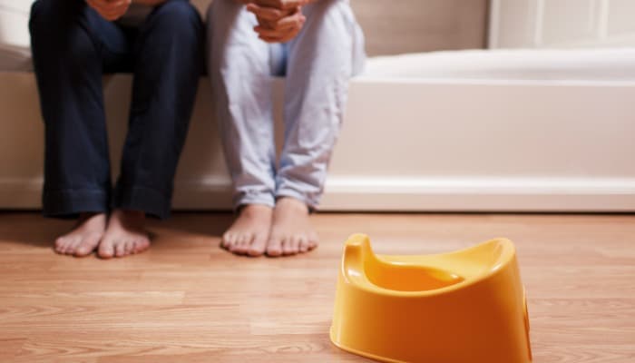 Potty training a stubborn toddler - potty seat sitting on a bathroom floor with parents in the background.