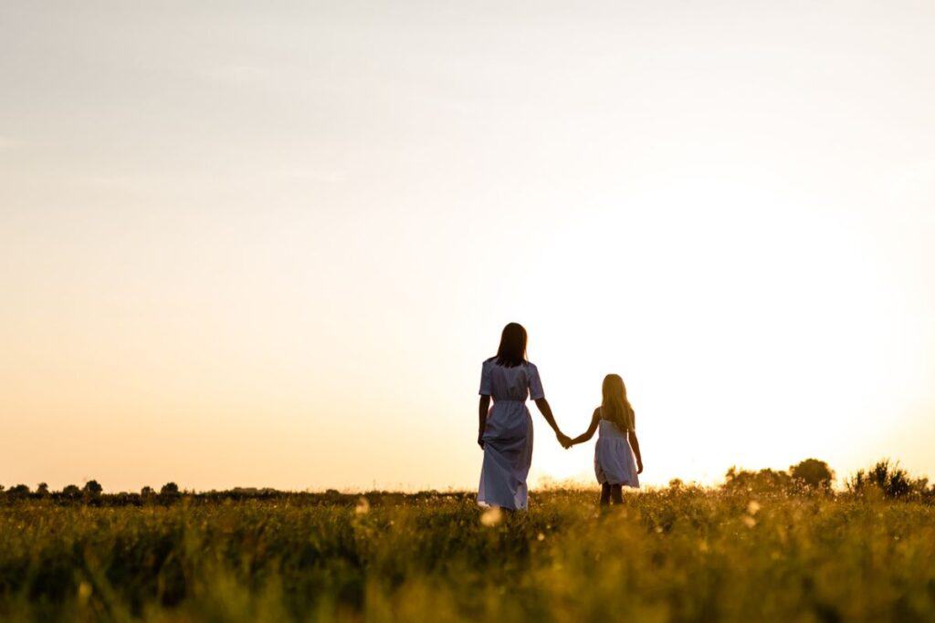 Woman with daughter in a field walking side by side.
