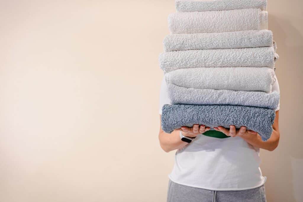 Woman holding a stack of freshly laundered bath towels in front of her.