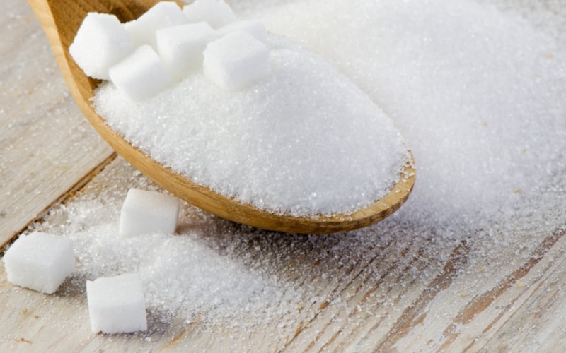 A wooden spoon overflowing with sugar and sugar cubes over a wooden table.