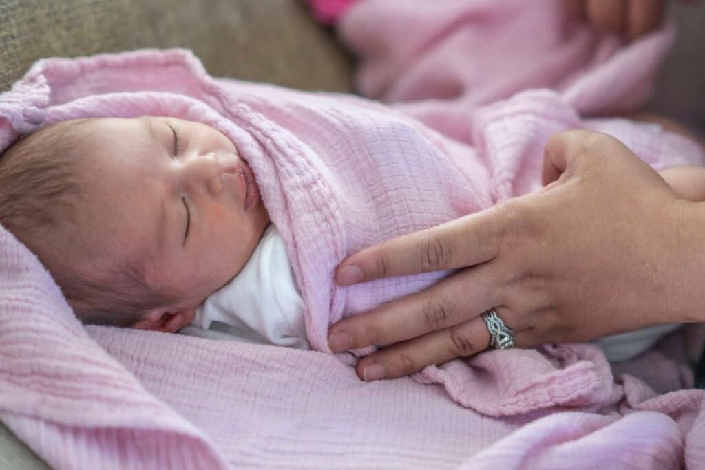 newborn wrapped in pink muslin swaddle.
