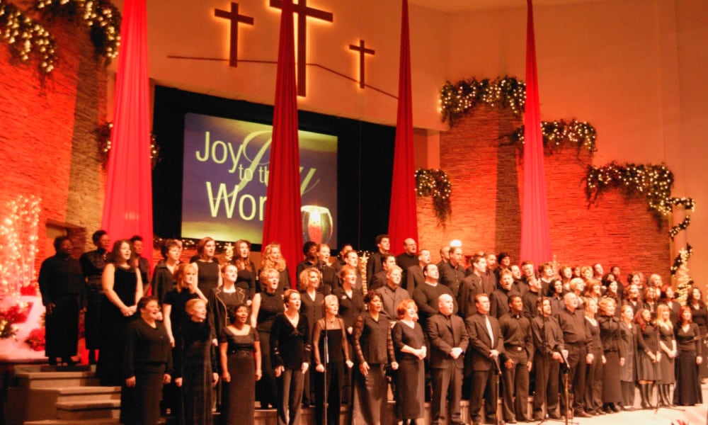 Christmas eve traditions - church service featuring a large choir singing Christmas songs with Christmas decor on the stage.