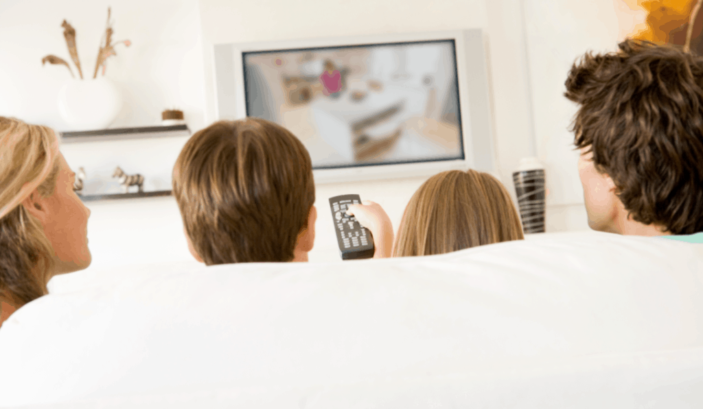 Teaching patience to a digital generation: a family of four sitting on a white couch, watching TV