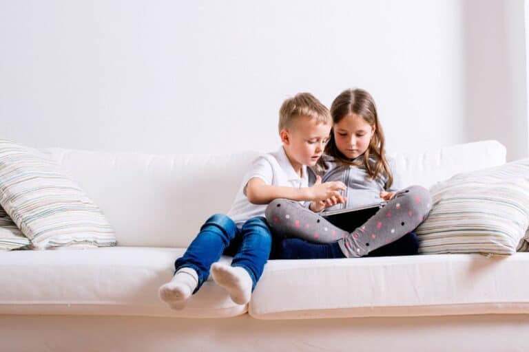 two siblings using tablet on couch