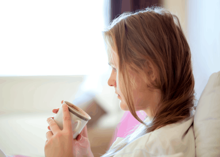 mom with cup of coffee and messy hair, sitting on the couch and daydreaming.