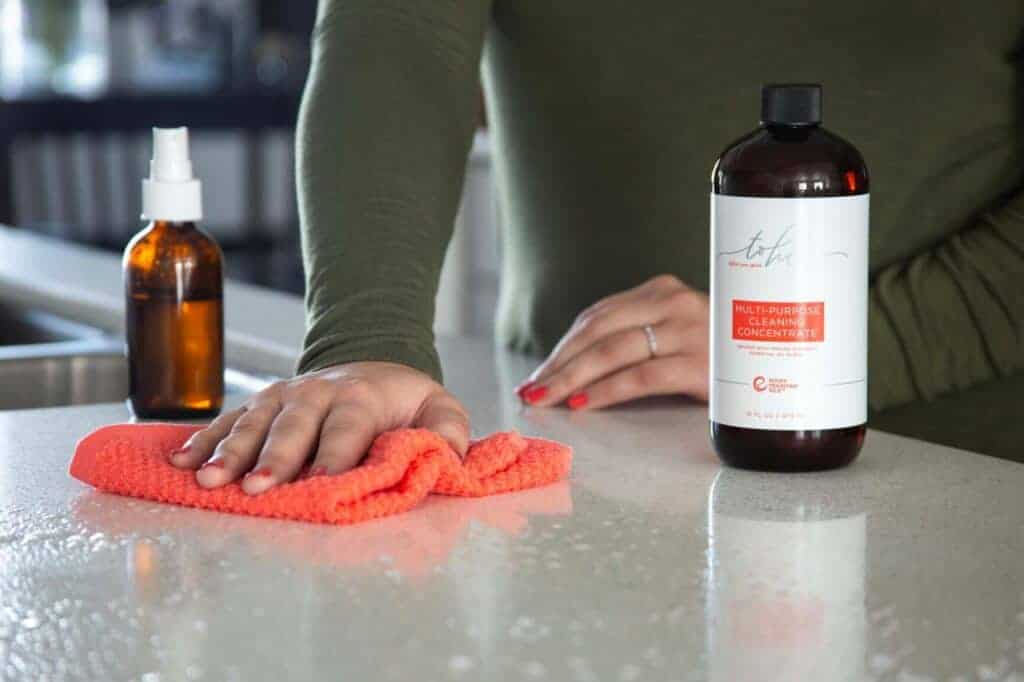 image of gift idea for homemakers: multipurpose cleaner on a kitchen countertop with a woman scrubbing the countertops with a dishcloth.