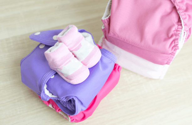 Stacks of colorful cloth diapers and baby booties on a wooden table.