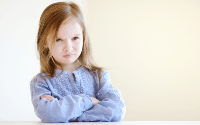 Pouting little girl in a blue shirt with arms crossed.
