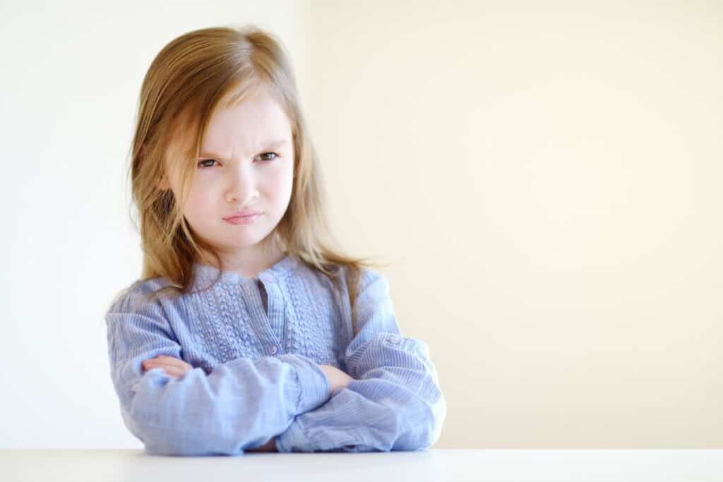 pouting little girl in a blue shirt with arms crossed.