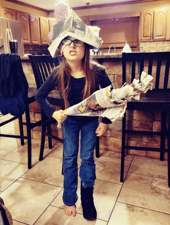 Image of preteen girl standing in kitchen with a newspaper pirate hat and newspaper sword. Concept of Indoor Activities for Kids - Newspaper Pirate Costume