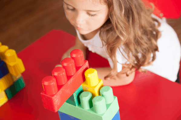 Image of grade-school aged girl stacking legos on a table - idea for indoor creative activities.