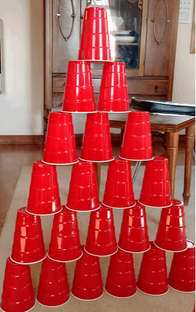 Image of red disposable cups stacked in a pyramid on the living room floor. Stacking cups: One idea for Indoor activities for Kids