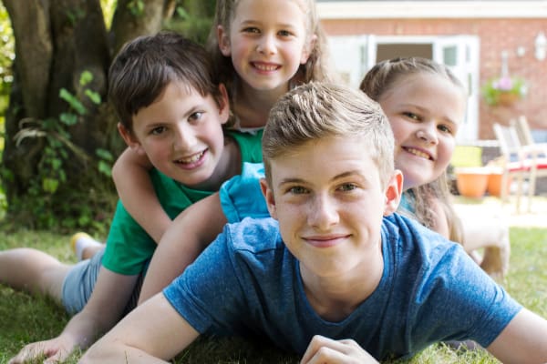 Image of four kids in a pile on the lawn, playing and smiling. Concept of considering- should I have four kids.