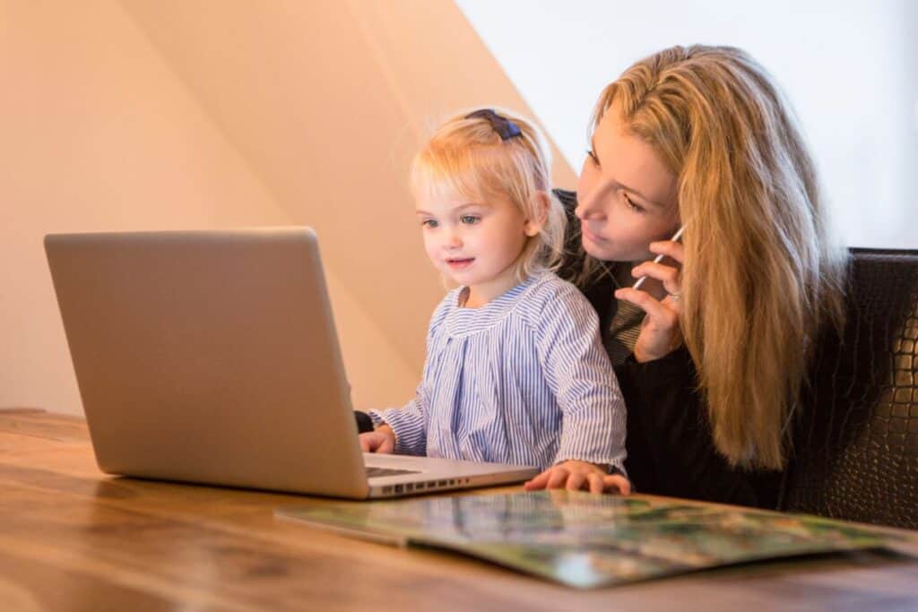 mom and toddler daughter in front of laptop at kitchen table.