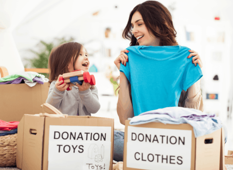 A mom and toddler daughter sorting clothing into boxes labeled Donation Toys and Donation clothes.