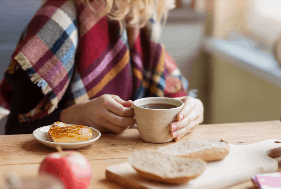 Woman sitting at a table with a cup of coffee and bread; concept of Bible verses about anxiety and worry for the anxious mom