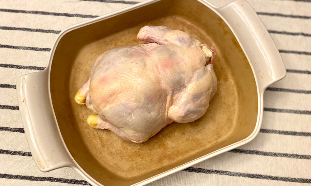 whole chicken in a baking dish, displaying step one- rinse and dry whole chicken