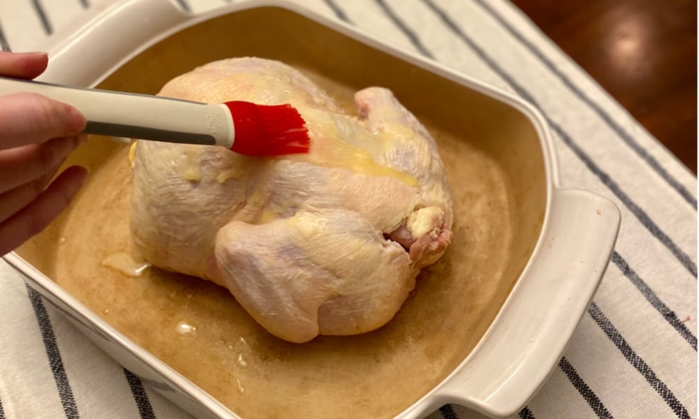 Demonstration of Using a basting brush to spread melted butter over whole chicken.