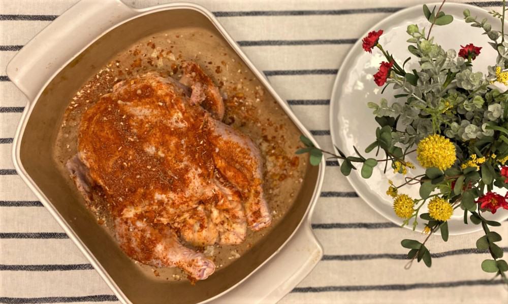 spice rubbed whole roasted chicken in a baking dish on kitchen table, just before baking.