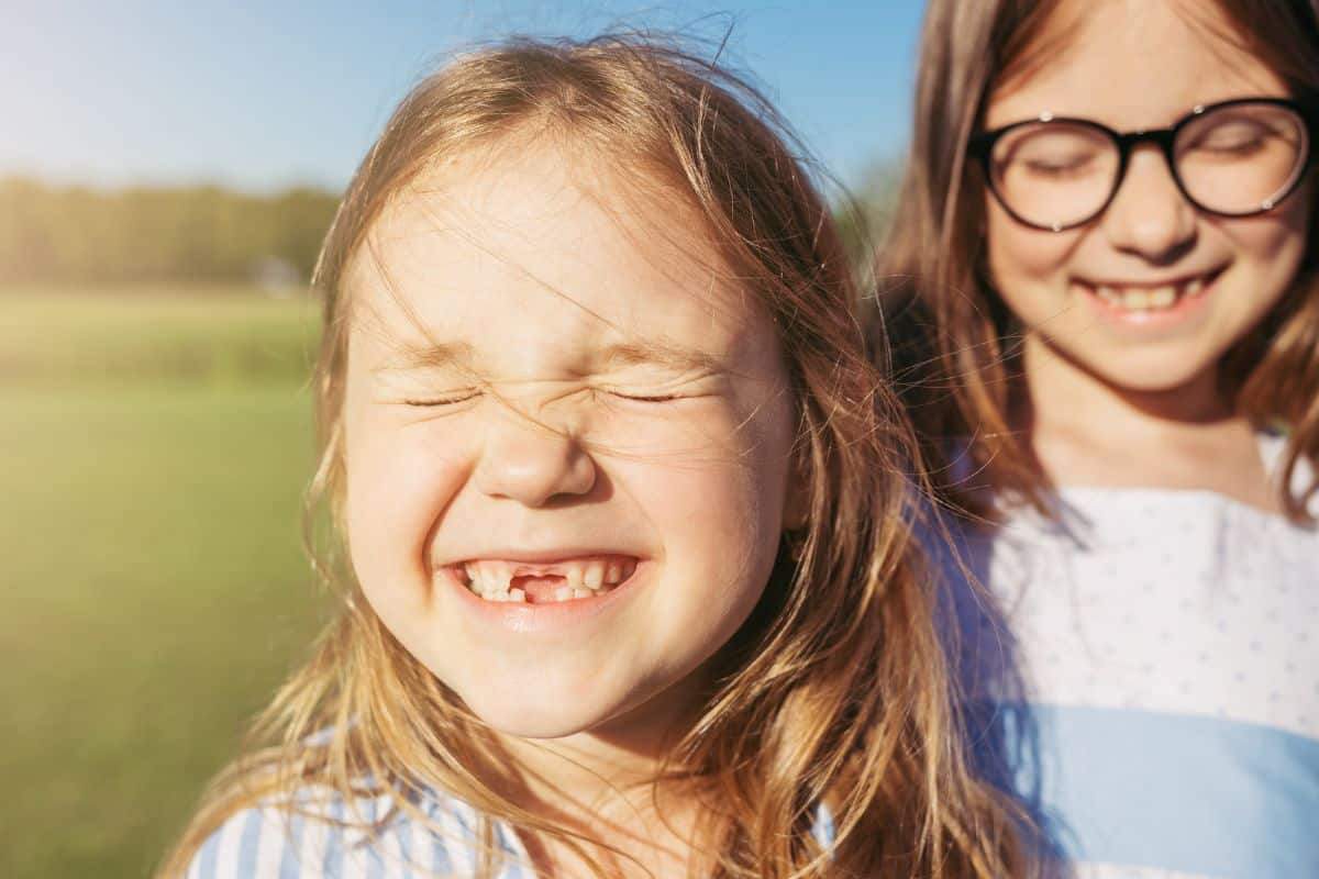 Two girls grinning in the sun outside.