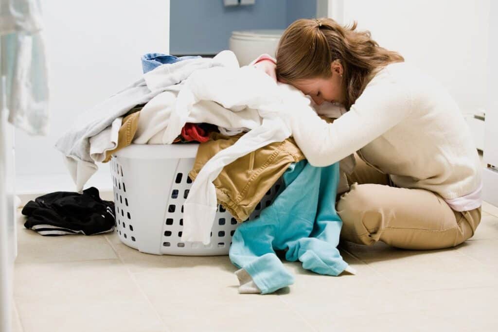 overwhelmed mom with head down in a pile of laundry.