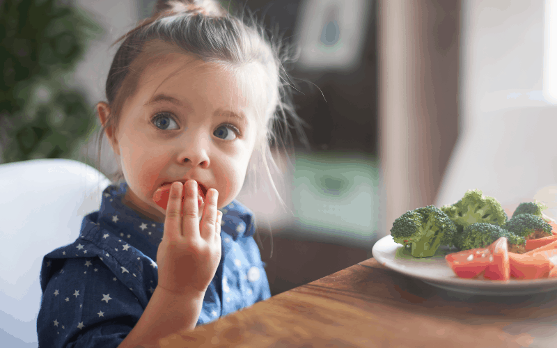 young girl eating vegetables: concept of Teaching kids responsibility at dinnertime