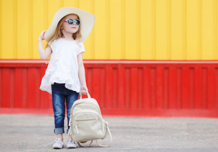 The trap of excess: image of young girl with a white oversized hat, fashionable outfit and leather backpack against a yellow and red background.