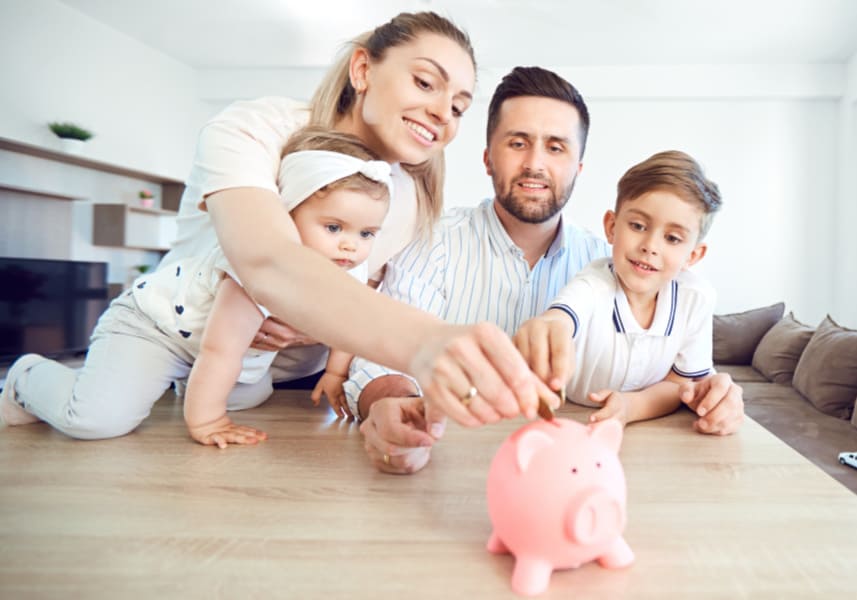 Why budgeting family expenses is key to avoiding overindulgent parenting: a family of four putting coins in a piggy bank on the coffee table at home.