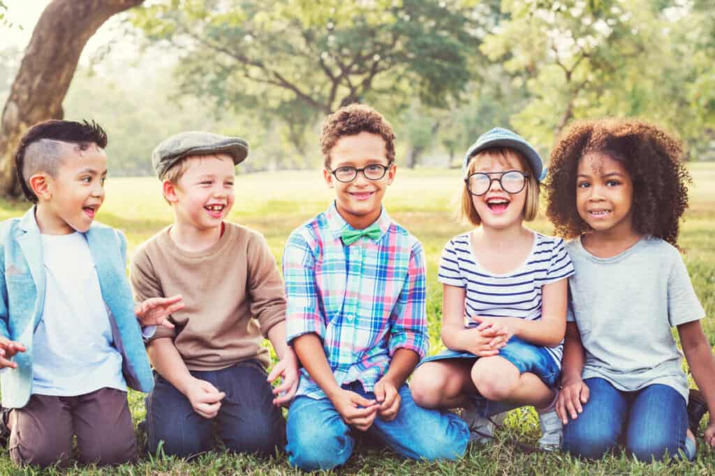 Group of smiling kids sitting together outside under a tree.