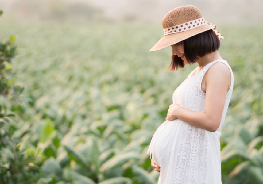 Pregnant mom looking down at her baby bump in a beautiful green field; concept of sanctity of human life- podcasts for Christian women and moms