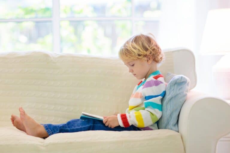 Little girl sitting on couch reading a book.