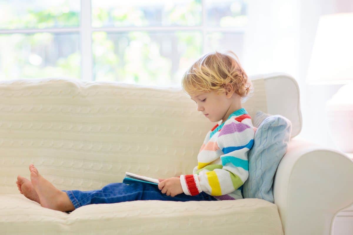 Little girl sitting on couch reading a book.
