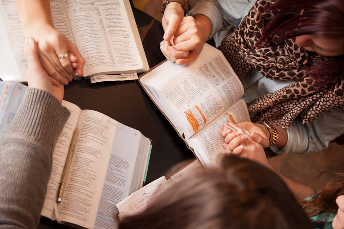 Women gathered around praying with their Bibles open on table.