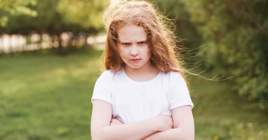 pouting tween girl standing outside with arms crossed