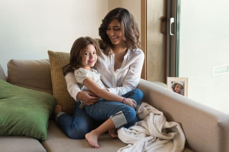 Mom and daughter cuddling on couch.