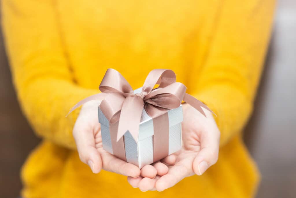 Woman in yellow sweater holding out a small gift box.