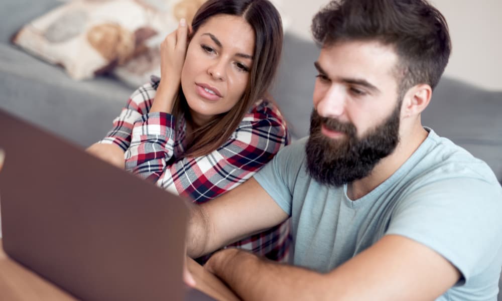 Young couple sitting by the coffee table with a laptop; concept of budgeting your money each month.