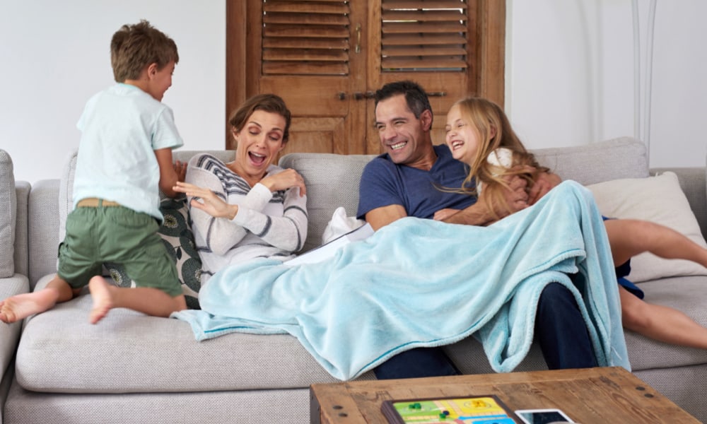 Mom, dad and two kids laughing on a couch together: concept of improve family finances by spending more time together at home.