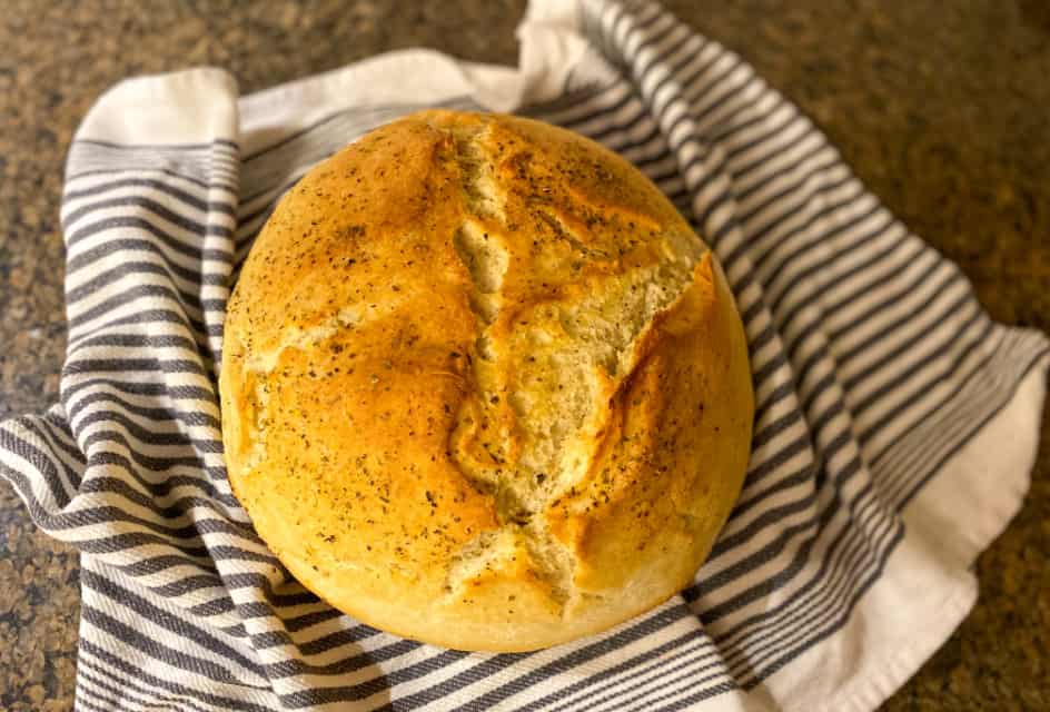 Ready to eat crusty french bread recipe - round artisan loaf on a striped tea towel resting on the counter.