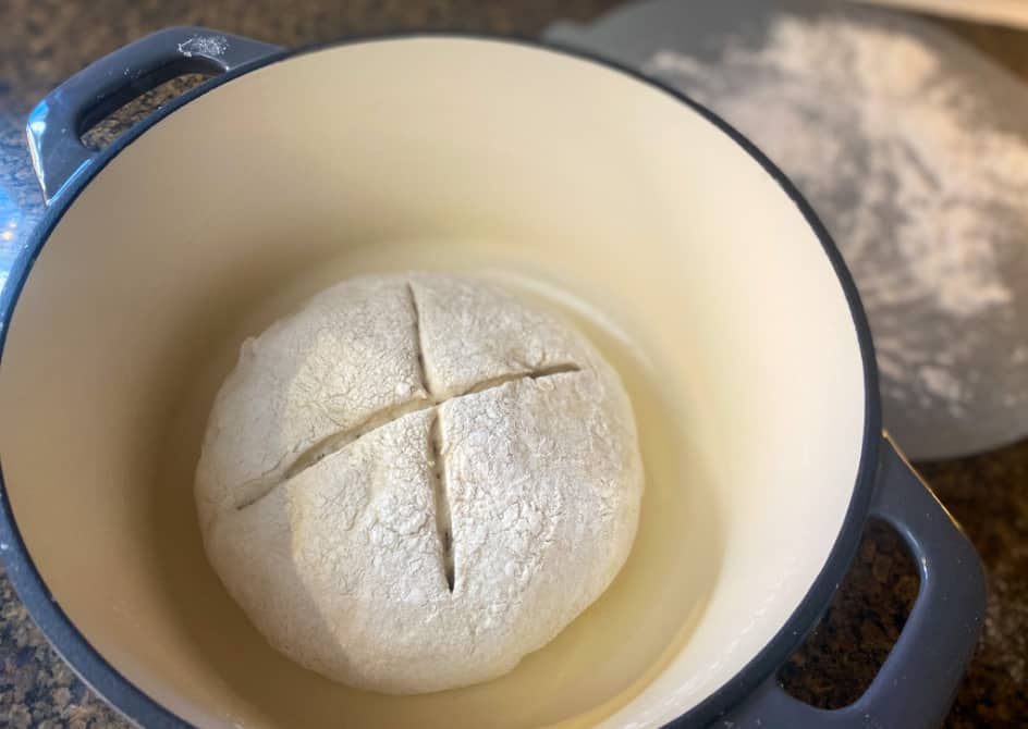 rustic dinner bread in dutch oven with x marked in middle, before baking.
