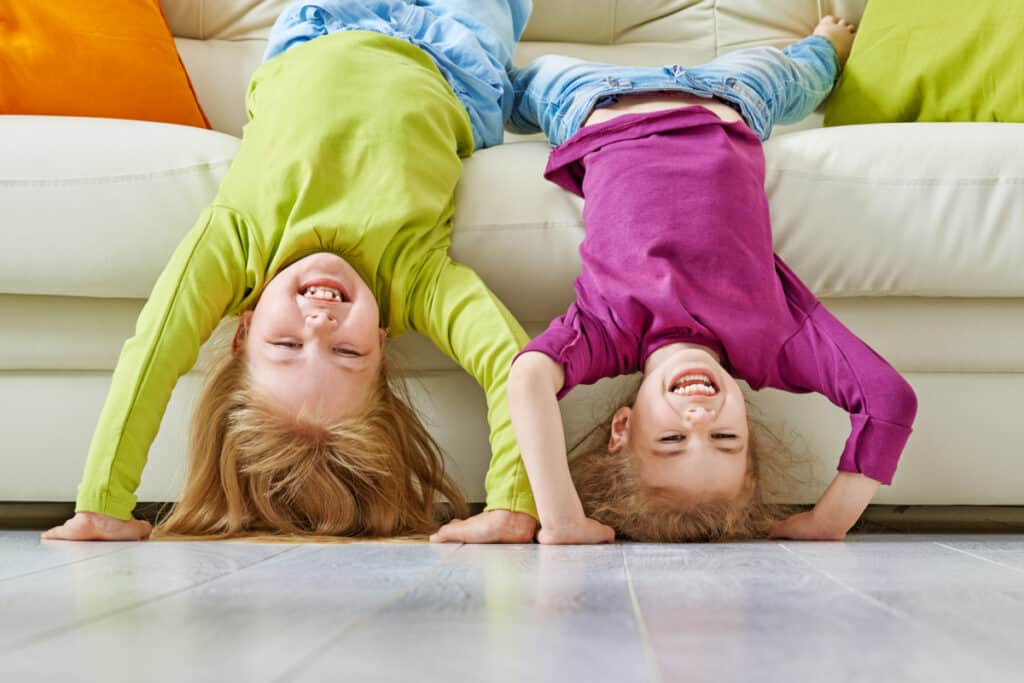 Two kids hanging upside down over a couch, laughing.